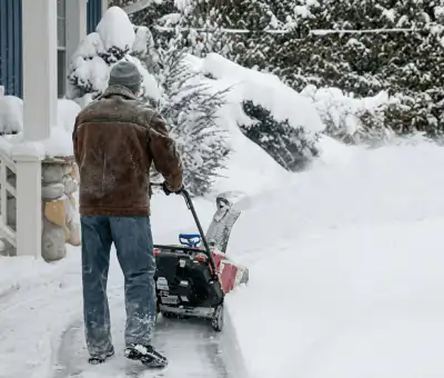 Residential snow removal technician using a snow blower to clear a home driveway and walkway in Aurora, IL
