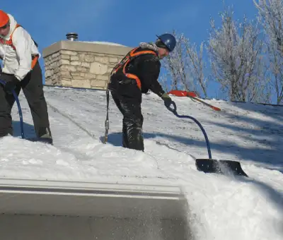 Professional technicians performing roof snow removal with safety harnesses and shovels in Aurora, IL
